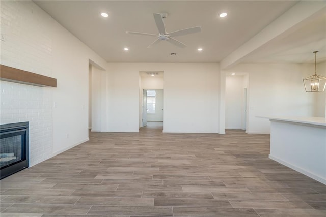 unfurnished living room featuring a fireplace and ceiling fan with notable chandelier