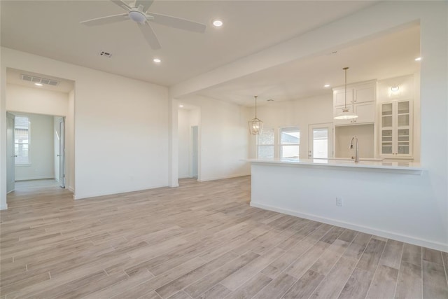 unfurnished living room with ceiling fan with notable chandelier, a healthy amount of sunlight, and light wood-type flooring