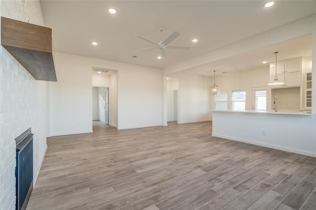 unfurnished living room featuring a fireplace, light wood-type flooring, ceiling fan, and sink