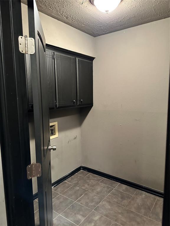 laundry area with washer hookup, cabinets, dark tile patterned floors, and a textured ceiling