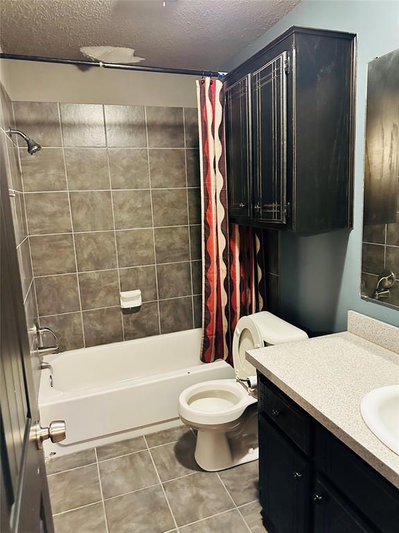 full bathroom with vanity, a textured ceiling, shower / bathtub combination with curtain, tile patterned flooring, and toilet