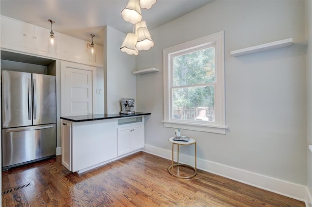 kitchen featuring stainless steel fridge, white cabinets, hanging light fixtures, and dark hardwood / wood-style floors