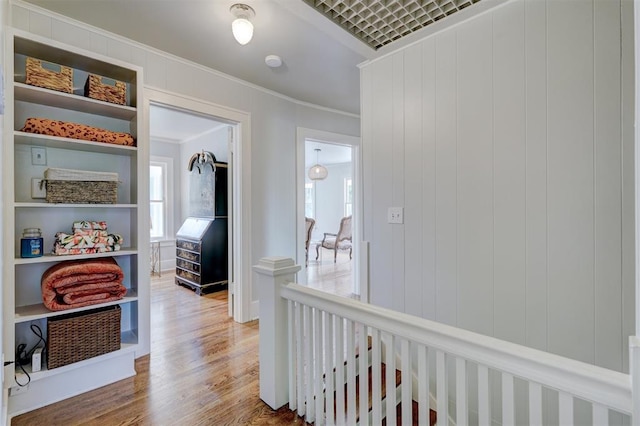 hall with wood walls, wood-type flooring, and ornamental molding