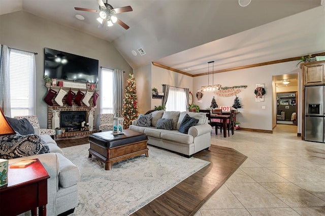 living room with ceiling fan, vaulted ceiling, a fireplace, light tile patterned floors, and ornamental molding