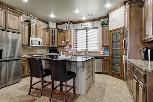 kitchen featuring a breakfast bar, crown molding, light stone countertops, appliances with stainless steel finishes, and a kitchen island