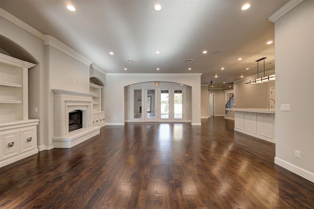 unfurnished living room featuring ornamental molding, built in features, and dark wood-type flooring