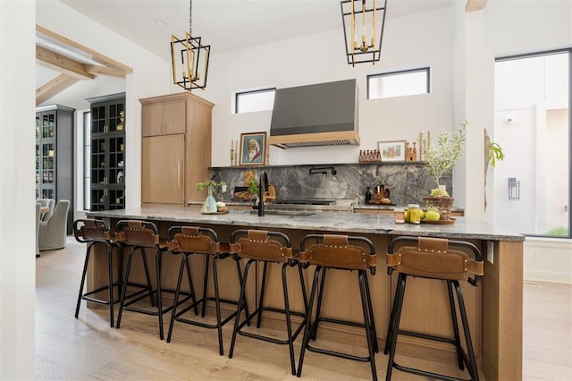 kitchen with tasteful backsplash, beamed ceiling, decorative light fixtures, light stone counters, and custom range hood