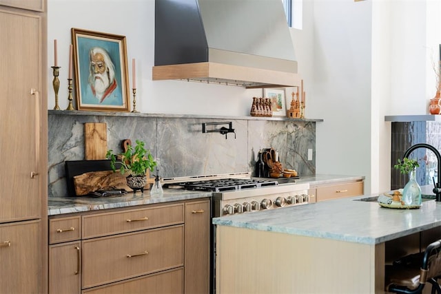 kitchen featuring wall chimney exhaust hood, light stone countertops, backsplash, and high end stainless steel range