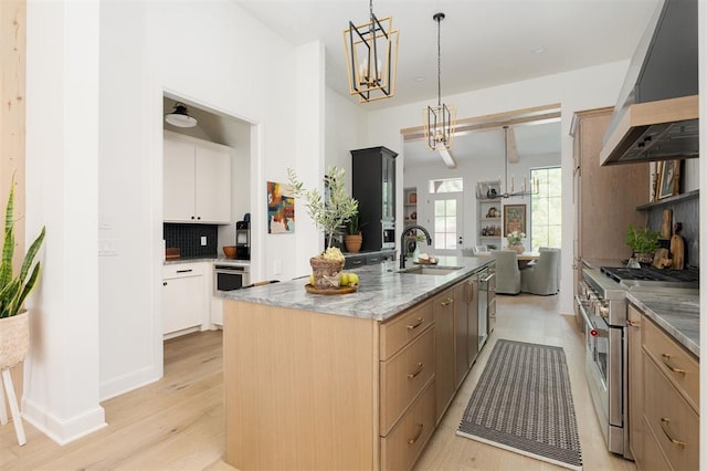 kitchen with wall chimney exhaust hood, stainless steel appliances, sink, white cabinetry, and an island with sink