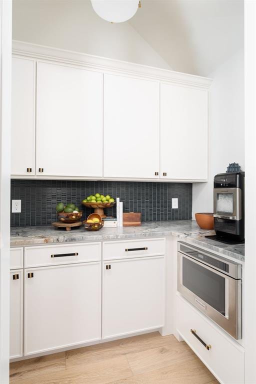 kitchen featuring white cabinets, stainless steel oven, tasteful backsplash, and light hardwood / wood-style flooring