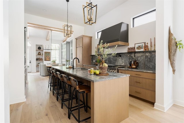 kitchen featuring hanging light fixtures, light wood-type flooring, extractor fan, and a kitchen island with sink