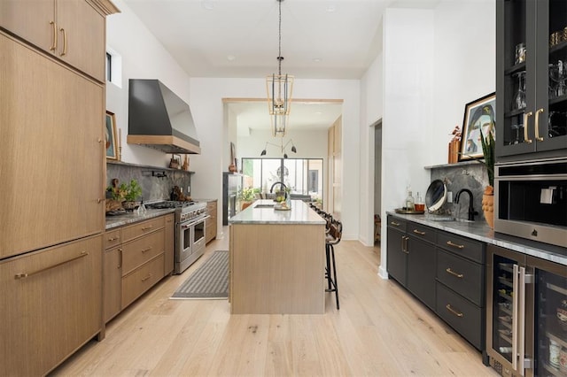 kitchen with wall chimney exhaust hood, stainless steel appliances, pendant lighting, a center island with sink, and a breakfast bar area