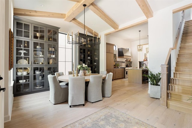 dining room featuring vaulted ceiling with beams, light wood-type flooring, and a notable chandelier