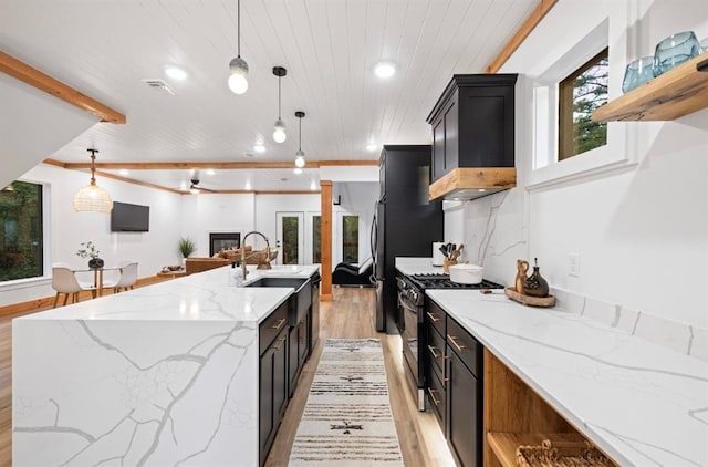 kitchen with beam ceiling, gas stove, pendant lighting, and light stone counters