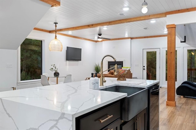 kitchen with light hardwood / wood-style flooring, a kitchen island with sink, light stone counters, a fireplace, and decorative light fixtures