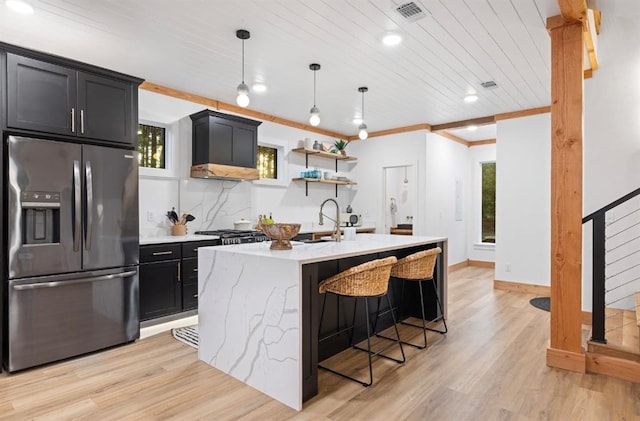 kitchen featuring stainless steel fridge, a kitchen island with sink, a kitchen breakfast bar, decorative light fixtures, and wooden ceiling