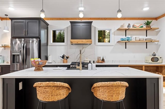 kitchen featuring pendant lighting, stainless steel refrigerator with ice dispenser, light stone countertops, custom range hood, and a center island with sink