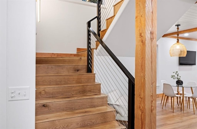 staircase with wood-type flooring and beamed ceiling