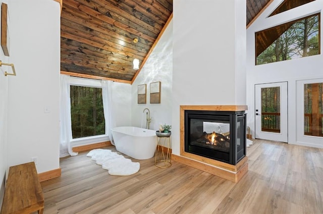 bathroom featuring wood ceiling, a bath, high vaulted ceiling, a multi sided fireplace, and hardwood / wood-style floors