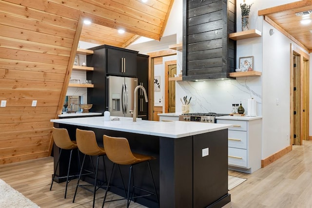 kitchen featuring a kitchen breakfast bar, stainless steel appliances, light hardwood / wood-style flooring, wooden ceiling, and an island with sink