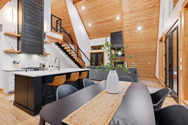 dining area featuring light wood-type flooring, wooden ceiling, high vaulted ceiling, and wooden walls