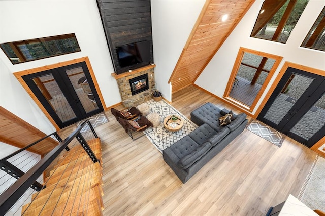 living room featuring a stone fireplace, light hardwood / wood-style flooring, a towering ceiling, and french doors