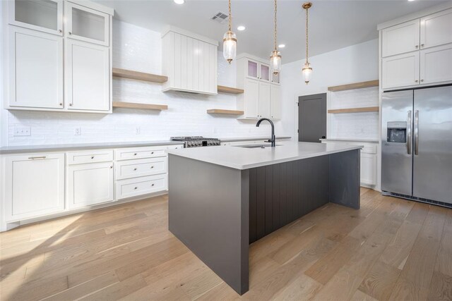 kitchen with stainless steel appliances, sink, white cabinets, light hardwood / wood-style floors, and an island with sink