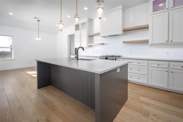 kitchen with light hardwood / wood-style flooring, white cabinetry, a center island with sink, and sink