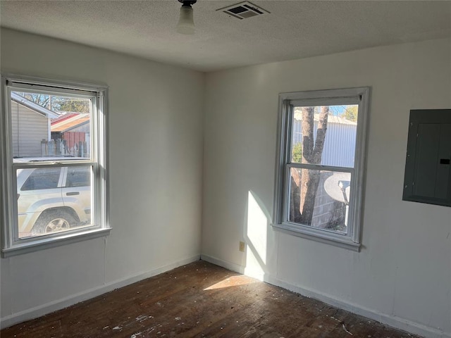 unfurnished room featuring dark wood-type flooring, a textured ceiling, electric panel, and a healthy amount of sunlight