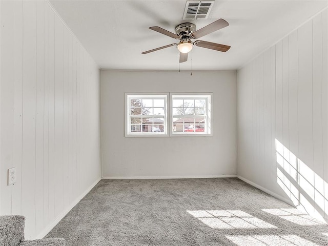 empty room featuring light colored carpet, ceiling fan, and wood walls