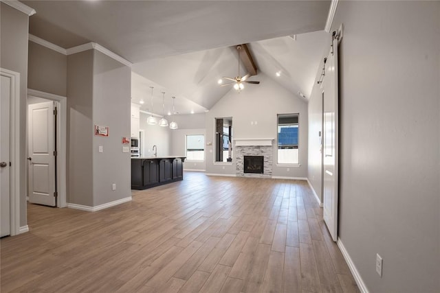 unfurnished living room with hardwood / wood-style floors, a stone fireplace, sink, ceiling fan, and beamed ceiling