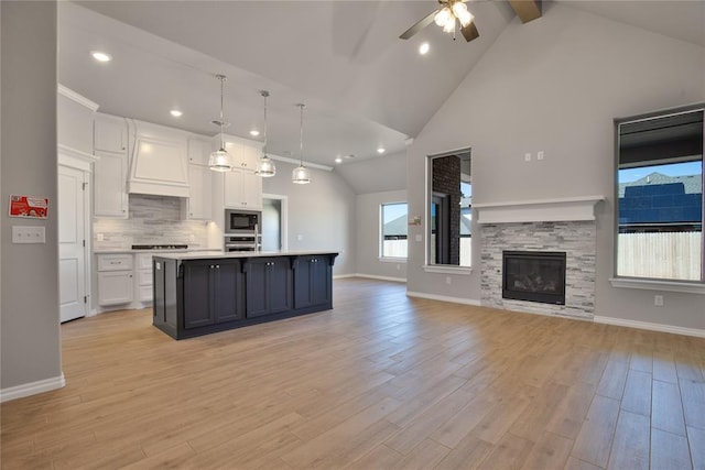 kitchen with built in microwave, white cabinetry, an island with sink, decorative light fixtures, and light wood-type flooring