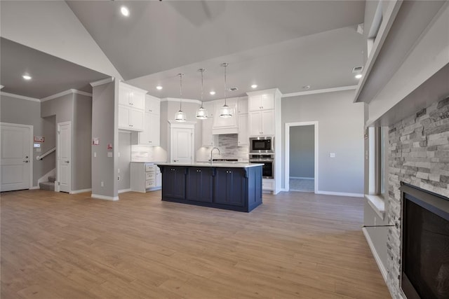 kitchen featuring a kitchen island with sink, decorative light fixtures, light hardwood / wood-style floors, white cabinetry, and a stone fireplace