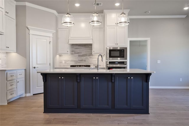 kitchen featuring appliances with stainless steel finishes, light hardwood / wood-style floors, a kitchen island with sink, and pendant lighting