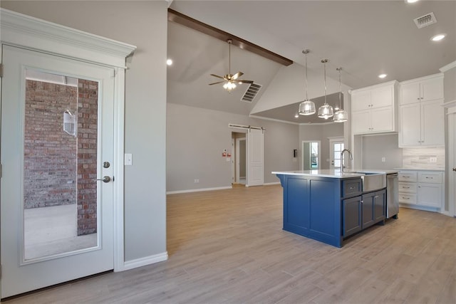 kitchen featuring white cabinets, a barn door, a center island with sink, and light hardwood / wood-style flooring