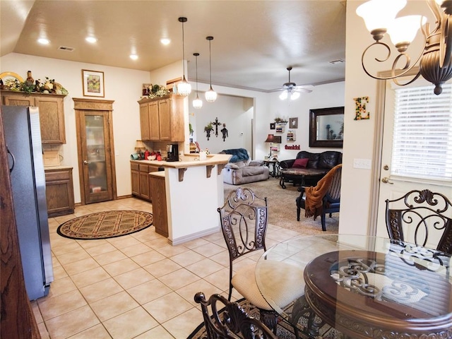 kitchen featuring pendant lighting, a kitchen breakfast bar, ceiling fan with notable chandelier, light tile patterned floors, and stainless steel refrigerator