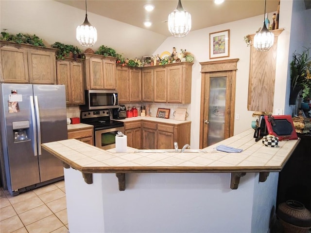 kitchen featuring decorative light fixtures, tile counters, a kitchen bar, kitchen peninsula, and stainless steel appliances