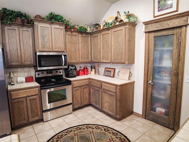 kitchen with tile counters, stainless steel appliances, tasteful backsplash, lofted ceiling, and light tile patterned flooring