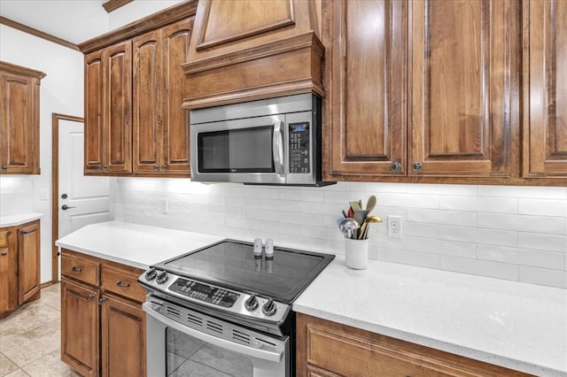 kitchen with light tile patterned flooring, ornamental molding, backsplash, and appliances with stainless steel finishes