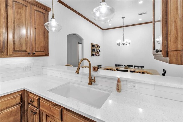 kitchen with sink, hanging light fixtures, tasteful backsplash, light stone counters, and crown molding