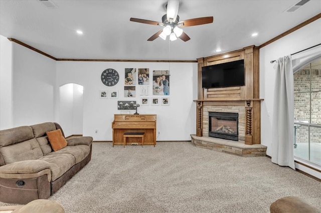 living room featuring carpet flooring, a stone fireplace, ceiling fan, and crown molding