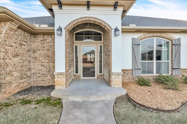 property entrance with a shingled roof, stone siding, brick siding, and stucco siding