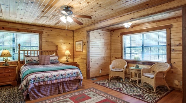 bedroom with hardwood / wood-style floors, multiple windows, wooden walls, and ceiling fan