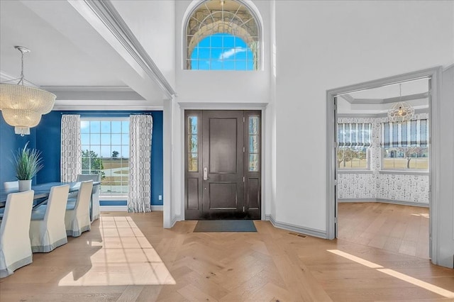 foyer entrance with light parquet flooring, a tray ceiling, crown molding, and a notable chandelier