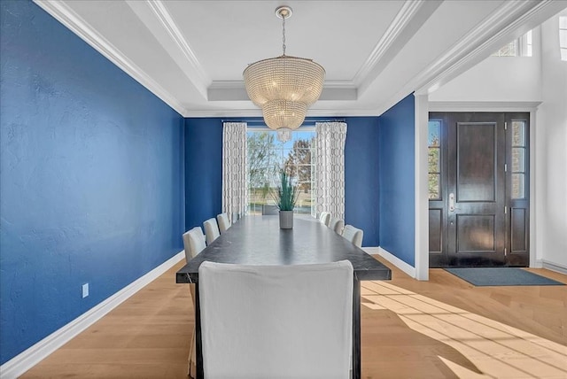 dining room with a chandelier, a raised ceiling, ornamental molding, and light hardwood / wood-style flooring