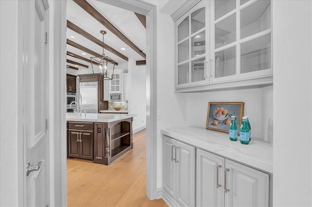 bar with dark brown cabinets, sink, built in appliances, light hardwood / wood-style flooring, and beamed ceiling