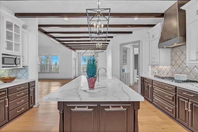 kitchen with pendant lighting, a center island with sink, wall chimney exhaust hood, beamed ceiling, and stainless steel appliances