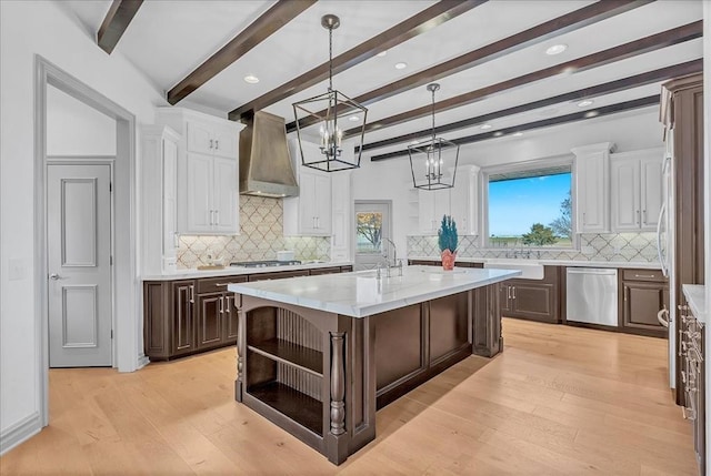 kitchen featuring a center island with sink, wall chimney exhaust hood, decorative backsplash, beamed ceiling, and stainless steel appliances