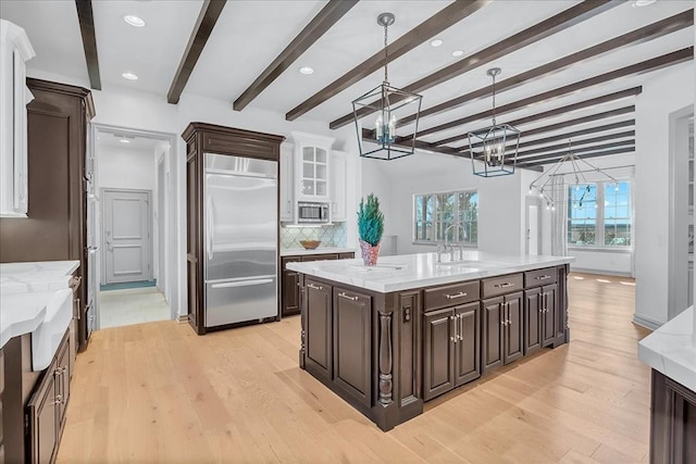 kitchen featuring beam ceiling, built in appliances, light hardwood / wood-style floors, and decorative light fixtures