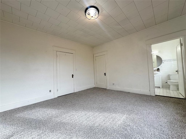 unfurnished bedroom with ensuite bathroom, carpet floors, tile walls, and a closet